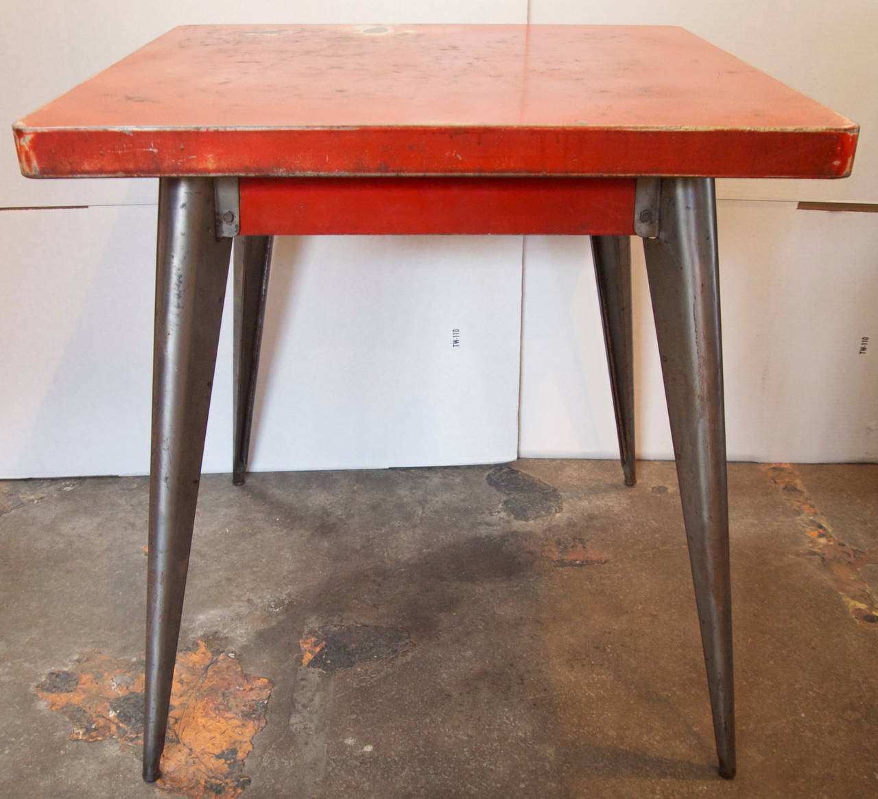 Wonderful French mid-century Tolix Industrial square metal bistro table with red patinated top and apron on stripped metal tapering legs