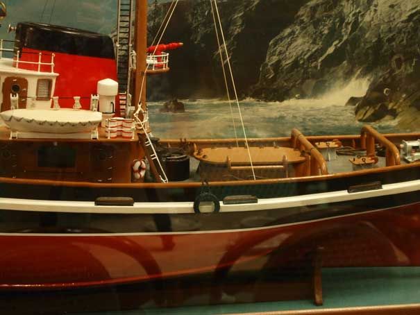Painted ship model 'Abeille' enclosed in glass case with dramatic background of the coast.