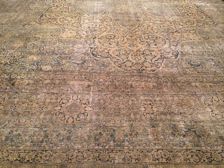 This very large, softly detailed Ravar Kerman antique rug presents a palette of taupe, black, gray, and cream. A border of highly segmented rosettes and floral motifs encloses a field of curling, swirling elaborate floral emblems.