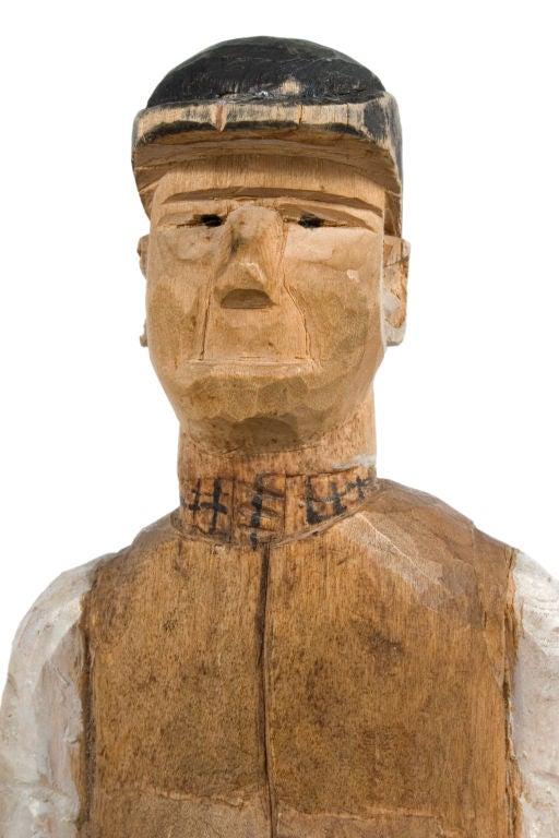 Painted wood carving of a man with a hat, a brown vest and striped pants.