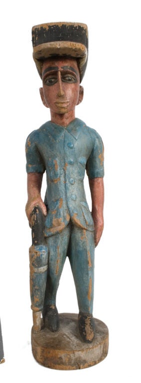 Carved wooden figure of a man in a blue outfit with an umbrella.