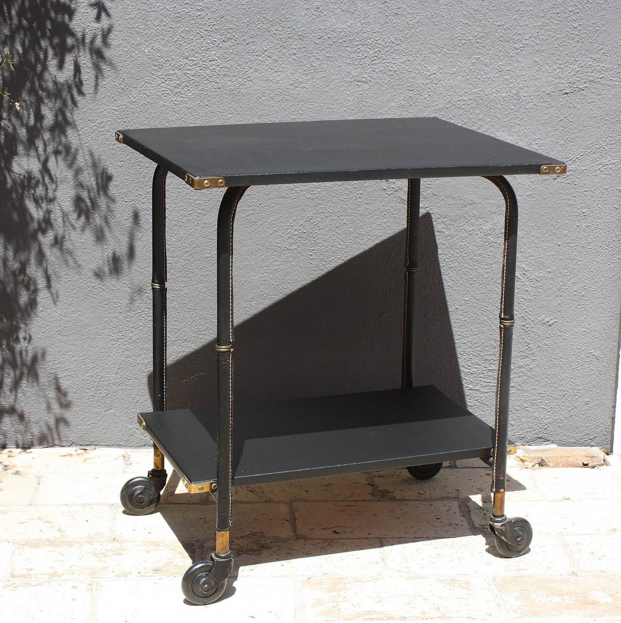 Jacques Adnet, rolling cart or trolley adjustable table with black lacquered metal covered with black (Piqué sellier), saddle stitch leather.
Top and shelf covered in black vinyl, typical of Adnet work.
Corner hardware and legs parts in