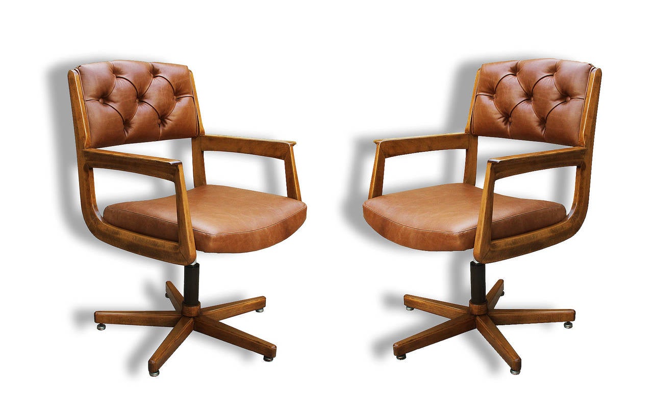 Rare to find and normally used for visitors, this beautiful pair of leather and beech wood swivel chairs has been reupholstered with a tan leather and button-tufting upholstery. The metal base is in its original condition and the wood has been