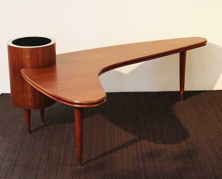 Maurice RINCK: Mahogany and Brass Coffee Table. 

Table top is in a boomerang shape with a brass bucket accessory at its corner for chilling champagne/beverages or placing flowers and other decorative items.

Table top and legs are in mahogany