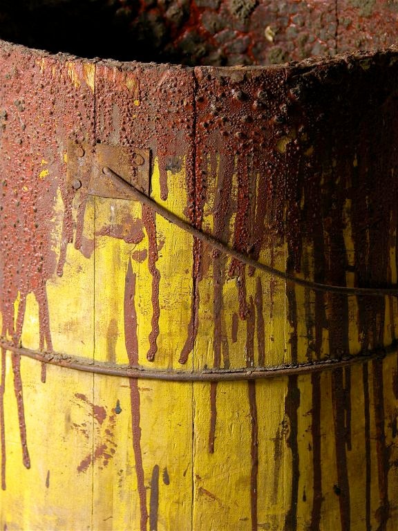 A yellow painted woodenware bucket encrusted in years of red paint use.