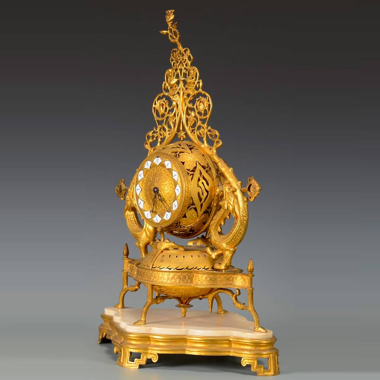 Gilt bronze French mantel clock with Chinese Chippendale feet
The circular dial with pierced sides and enamelled Arabic numerals flanked by dragons, pierced fretwork top and paw feet, resting on a shaped marble and gilt bronze base with Chinese