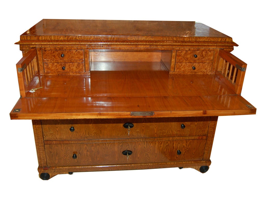 Biedermeier butler desk made of flamed birchwood, ebonized handles, brass keys. Drop front writing surface with interior drawers above three large exterior drawers.