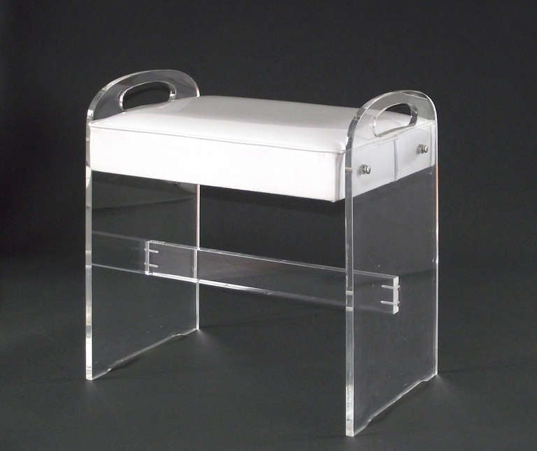 A lucite vanity stool with cross stretcher, integrated handles and its original, gloss-white vinyl upholstery.