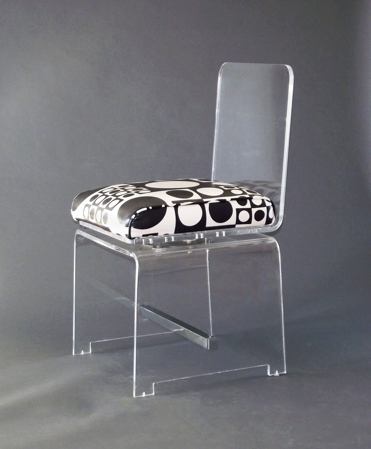 A vanity or desk chair comprising a waterfall base with chrome cross stretcher and end caps, upholstered in a graphic Op-Art vinyl fabric. The seat swivels a full 360 degrees and does so smoothly. *Please note: the lucite is perfectly clear - they
