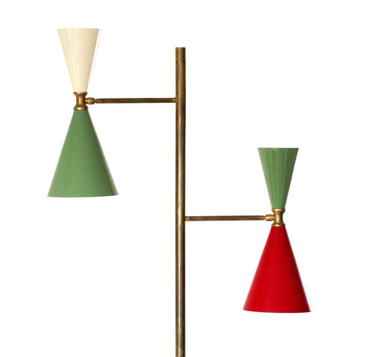 A classic, 1950s-style Italian floor lamp designed in the style of Stilnovo with brass base, upright and arms with applied antique/aged finish and two asymmetric, diabolo-shaped shades in enameled metal. Each shade has a socket at both ends and