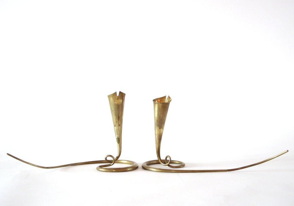 A pair of highly lyrical, solid brass candlesticks by American blacksmith/metal sculptor, Daniel Miller. Each was fashioned from a single piece of metal, meticulously worked from the fine 'tail' through the sinuous base and up to the trumpet-shaped