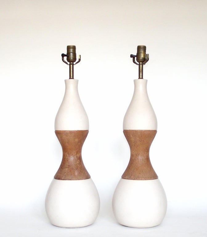 A tasteful pair of pottery table lamps in an hourglass form with the top and bottom segments in a subtly-textured, off-white, matte glaze and the middle section in faux bois (incredibly well-done, realistic to both the eye and to the
