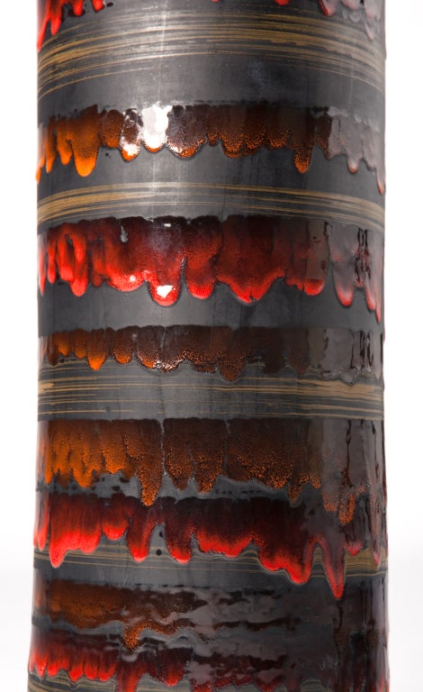 Tall, cylindrical pottery lamp by Bitossi with a matte black ground, gilded banding and a rich, drip glaze in fiery reds and oranges. Heavy, solid brass finial is finished in black to match the lamp body. Beautiful, graphic design, most likely a