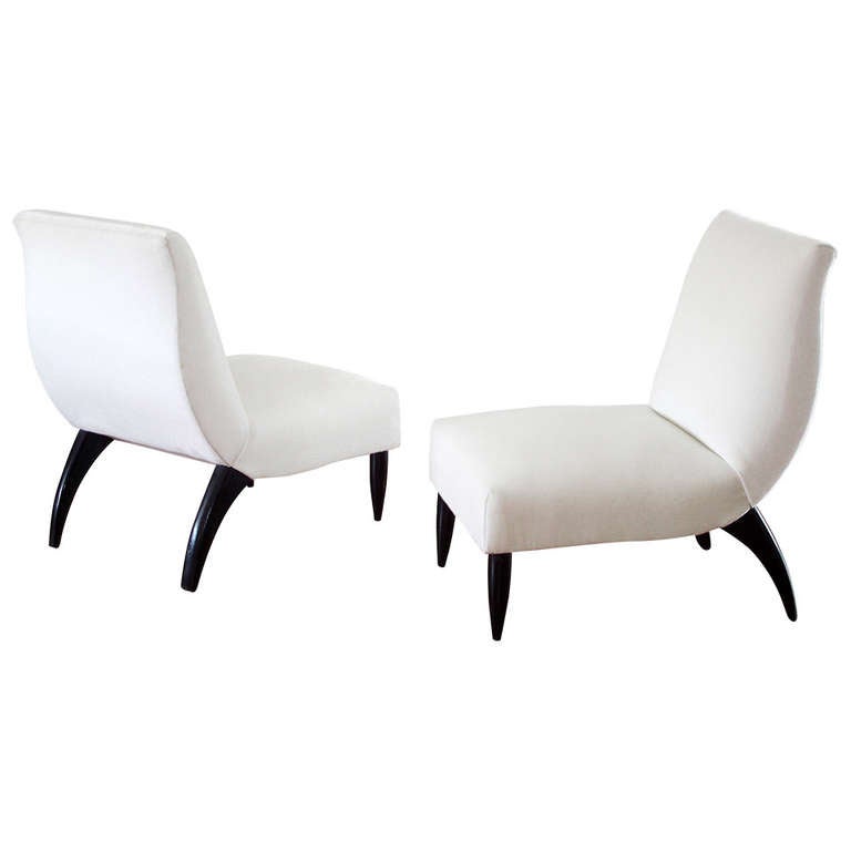 A pair of Italian slipper chairs with ebonized wood frames and new, imported, faux mohair upholstery in snow white. Tapering, vertical front legs juxtapose with curved and splayed rear legs that meet an undulant, hand-stitched backrest. Underside is