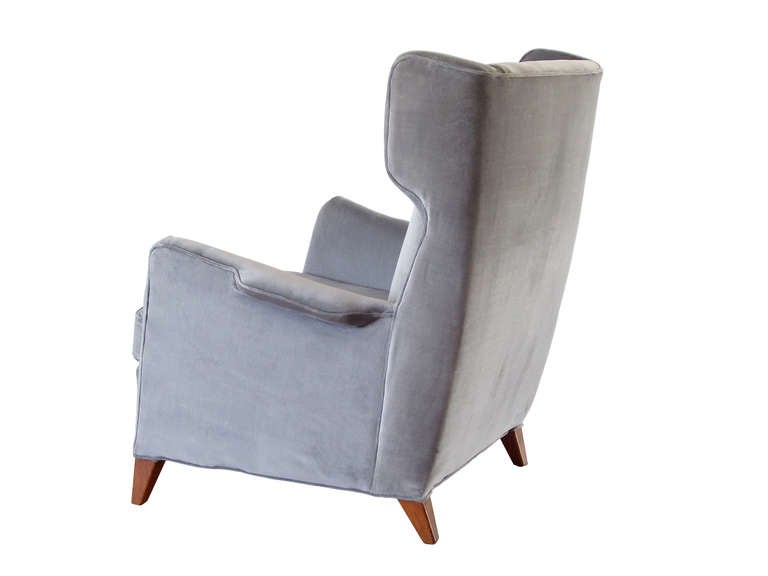 A modernist wingback chair with a handsome, crisply tailored frame supported by short, angular legs in mahogany, newly upholstered in a cool gray cotton velvet. In the manner of Dunbar ... with a faintly Italian flair.
