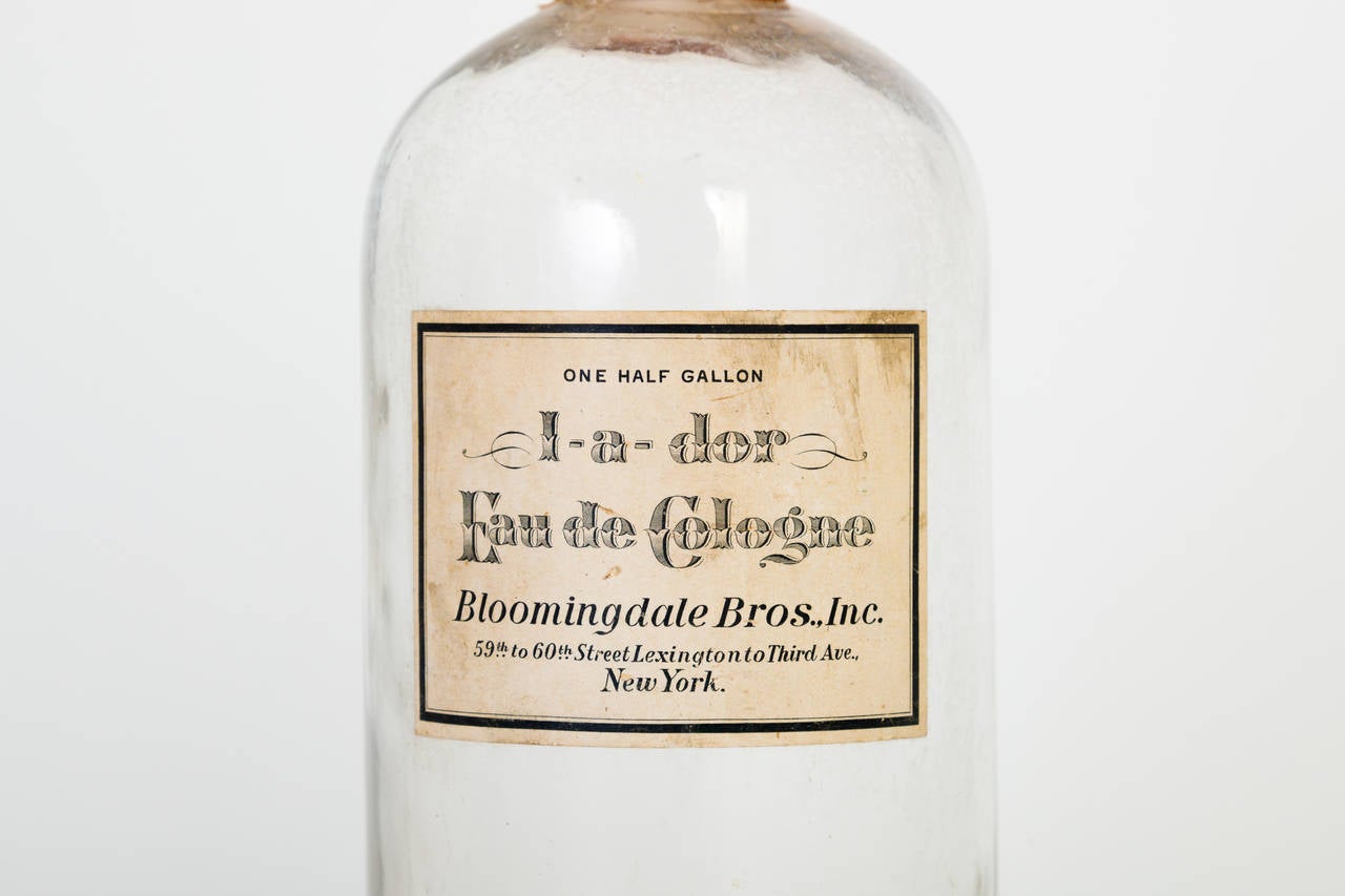 A scarce, Bloomingdale's half-gallon perfume bottle that was used for dramming individual bottles for retail sale of their 'I-a-dor' (I adore) cologne. All original, including the charming label that's fully intact, the stopper and its silk ribbon.