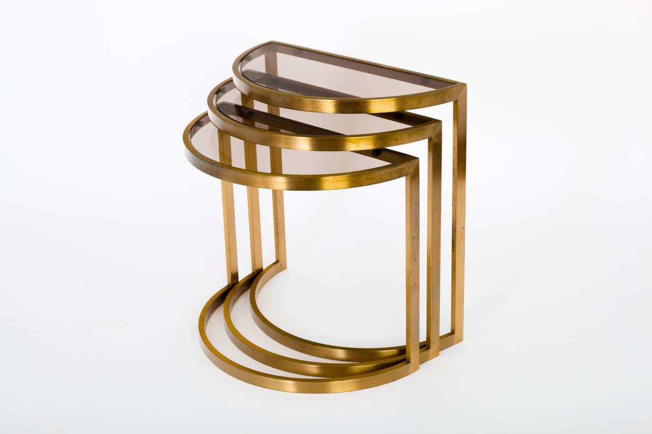 A set of three half-moon (demi-lune) nesting tables comprising flat bar frames in satin brass and inset, bronze-tinted glass tops. We believe these to have been manufactured by Metropolitan Furniture. Tastefully simple design. *Please feel free to