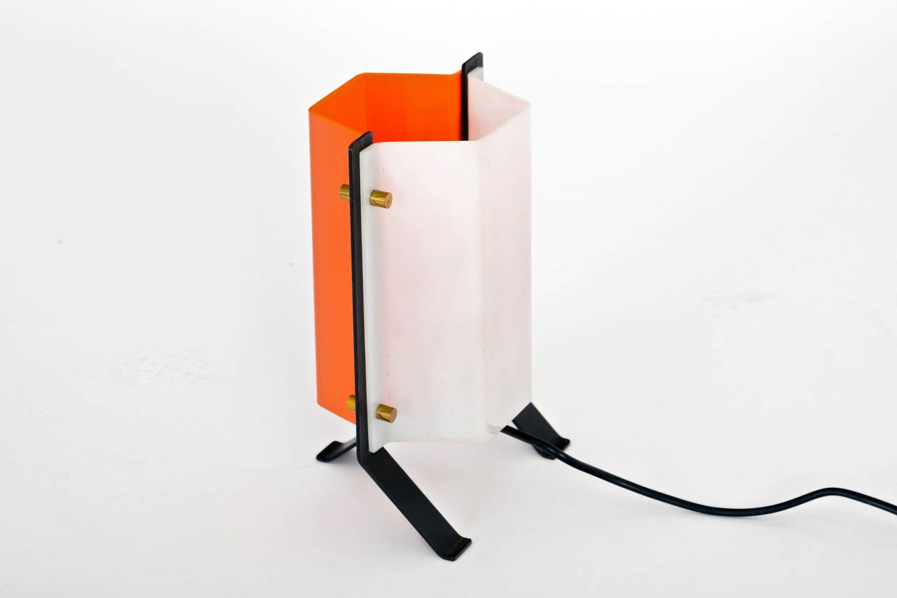 A playful little desk or table lamp that comprises an enameled, flat bar steel frame and integrated tripod base that supports two molded, acrylic panels in contrasting shades of white and red-orange, fastened together by cylindrical, solid brass