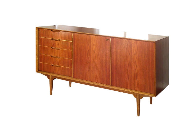 A fine Swedish Modern sideboard / buffet in bookmatched teak with a bank of five drawers to the left side and a pair of sliding doors to the right that reveal two adjustable shelves. A very well-crafted piece with wonderful attention to detail,