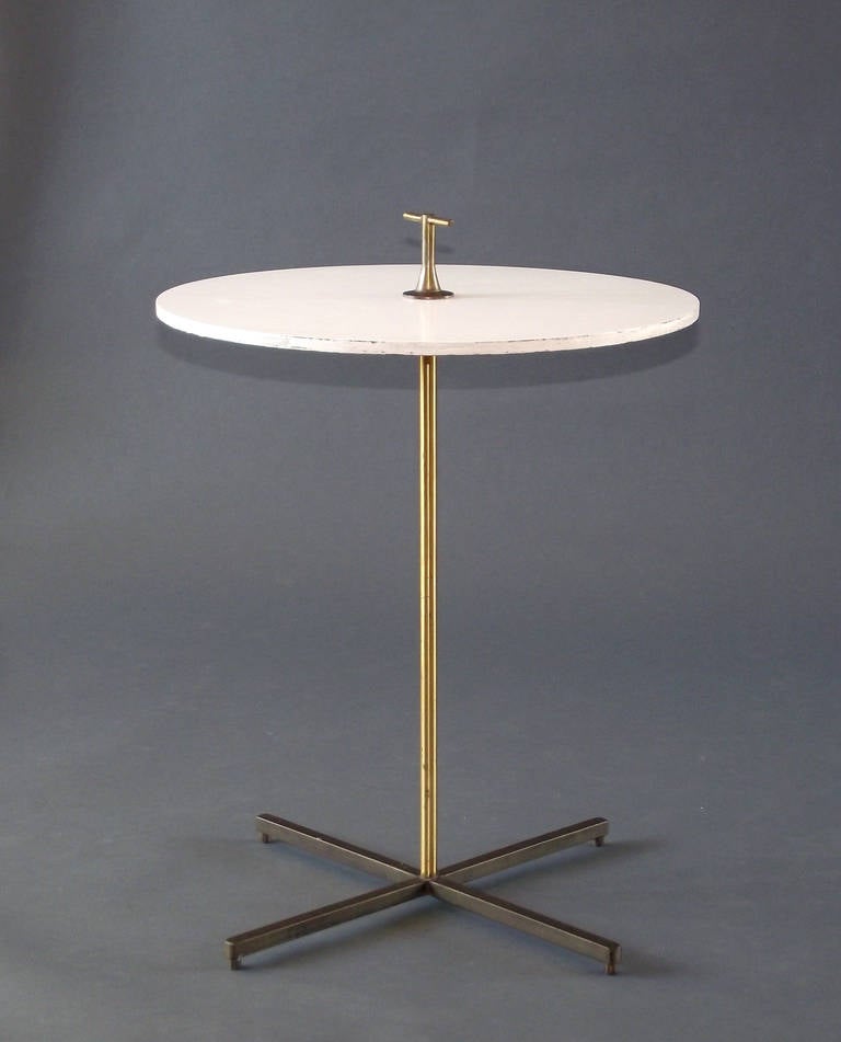 A delightful, modernist cigarette table in the spirit of Gio Ponti with a solid brass, X-shaped base, upright and decorative fitting supporting a painted/laminated wood tabletop. Wonderful patina throughout.