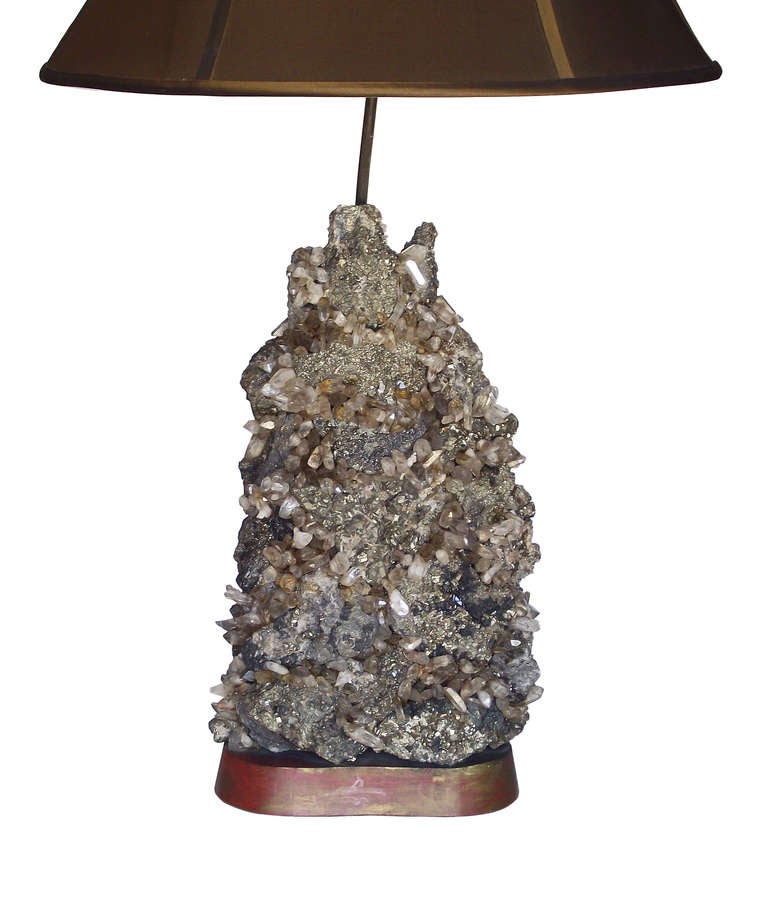A large-scale lamp by Carole Stupell comprising a dazzling cluster of pyrite and quartz crystals supported by a painted wood, biomorphic base and finished with a pyrite finial. The crystals are a mix of both clear and smoky with varying degrees of