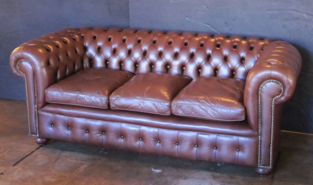 A fine English Chesterfield sofa in vintage brown leather featuring button-tufted back and arms, three soft leather fitted seat cushions, and beaded-nail trim design, resting on turned feet.

The Chesterfield sofa is a classic, synonymous with