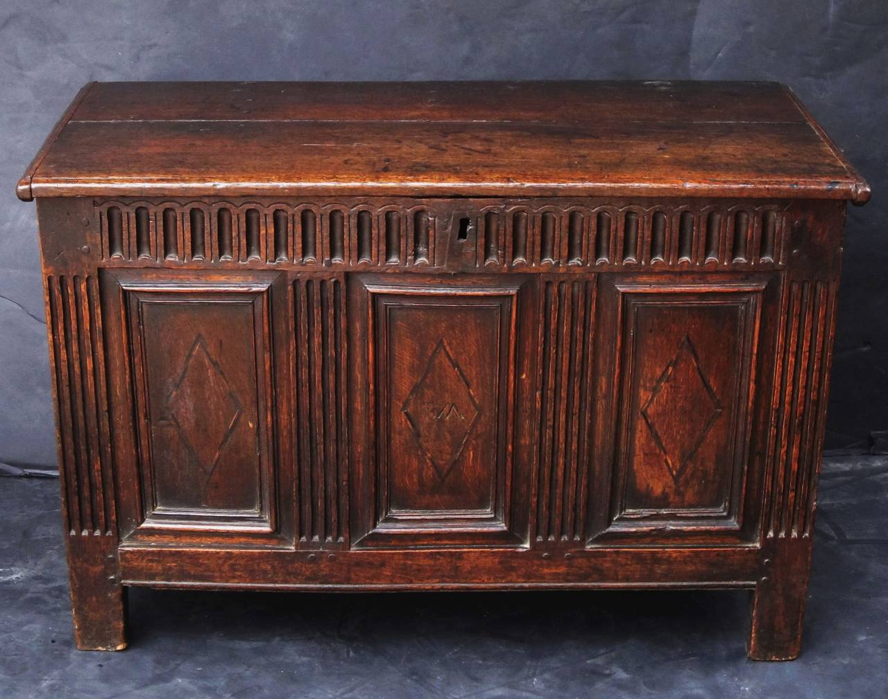 A handsome English panel carved coffer or chest (trunk) of oak from the Jacobean period (King James II), featuring an iron-hinged, panel top, mounted to a joined rectangular base. 

The base with a linen fold pattern along the top face, over three