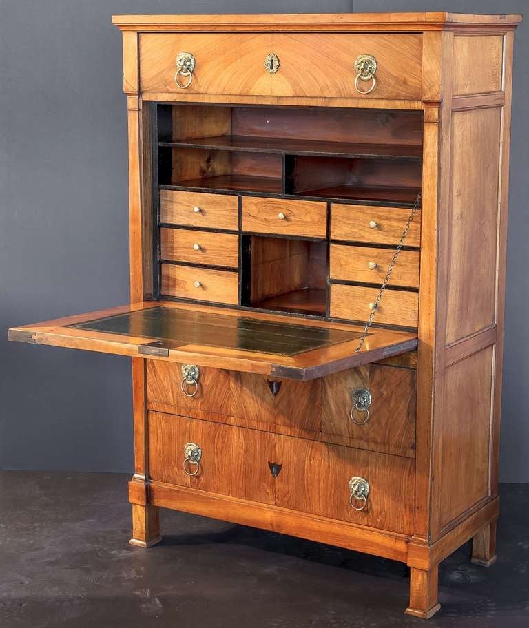 An exceptional French secretaire or secretary desk and chest of figured cherrywood, featuring a moulded top over a frieze of one long drawer with raised brass escutcheon and two brass lion pulls, the fall with inlaid ebony chevron escutcheon (and