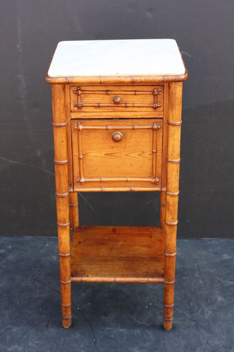 A French faux bamboo night stand (or commode) of long-leaf pine, featuring a white marble top over a frieze with drawer and cabinet fall attached to four turned legs and bottom tier. The whole accentuated by a faux bamboo design.

Perfect as a