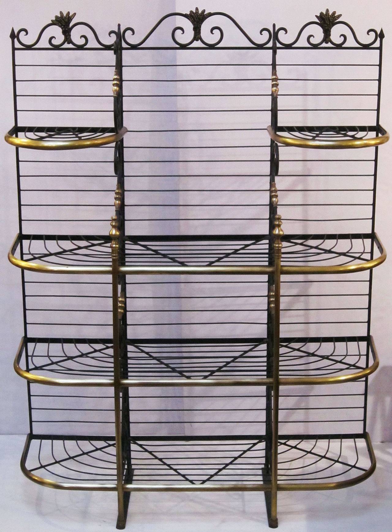 A large French baker's rack of wrought iron with decorative brass trim and finials, featuring scrolled dividing panels and four levels of shelves. 
The top frieze with ornamental sheaves of wheat and scroll-work back.