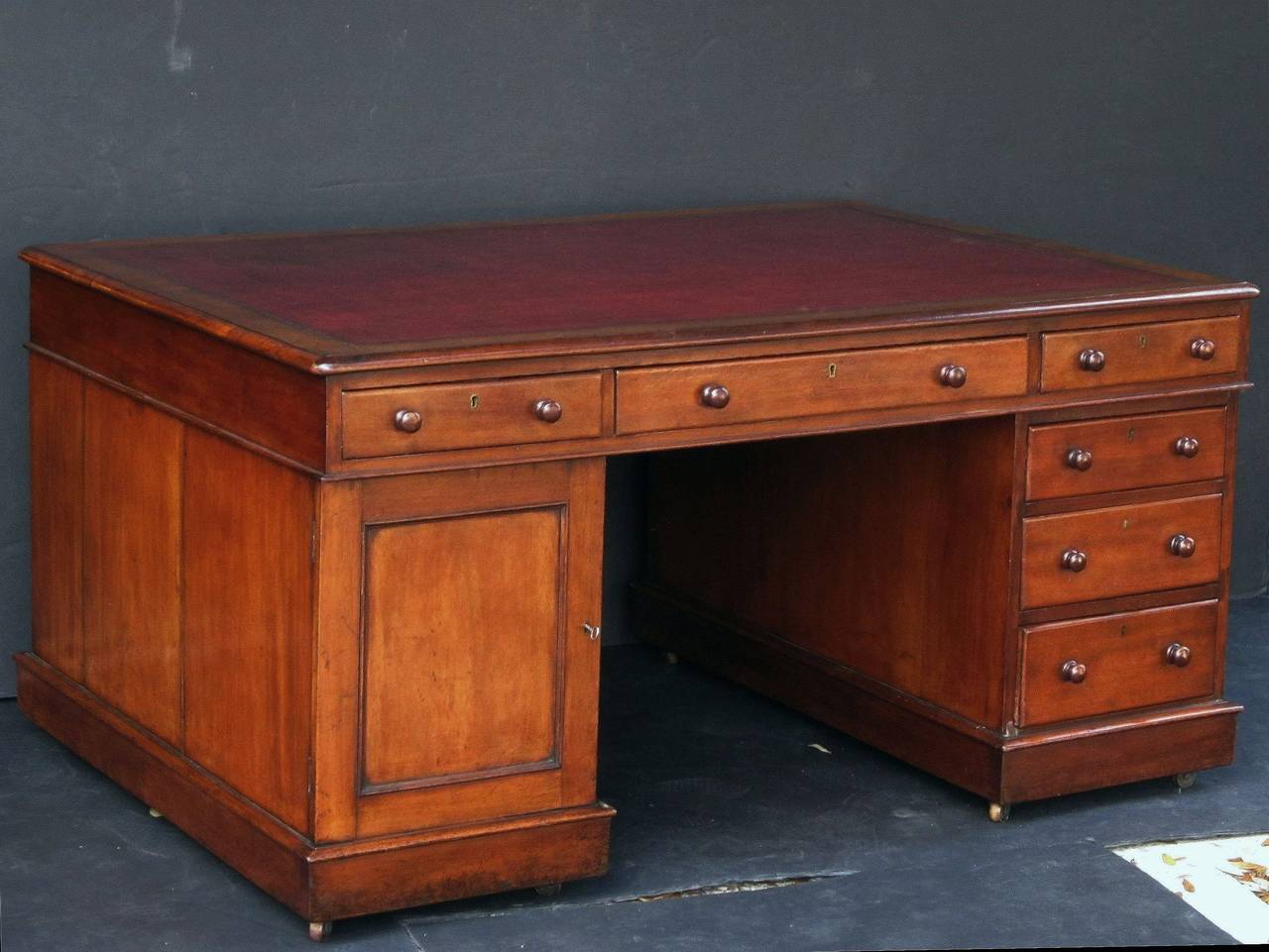 A handsome large English partner's desk of mahogany, featuring a moulded top inset with an embossed red leather, over a long drawer flanked by two short drawers on opposing sides. 
One pedestal with three short drawers resting on raised plinths and