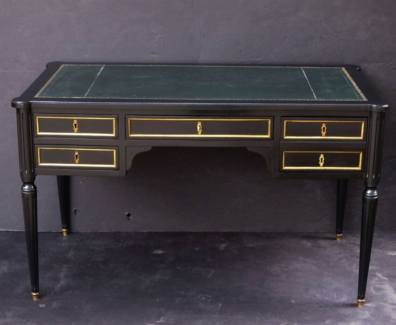An elegant French writing desk (or table) of ebonized mahogany, featuring an embossed leather top with gilt bronze accents over a frieze with recessed drawers and opposing faux drawers, with two 14