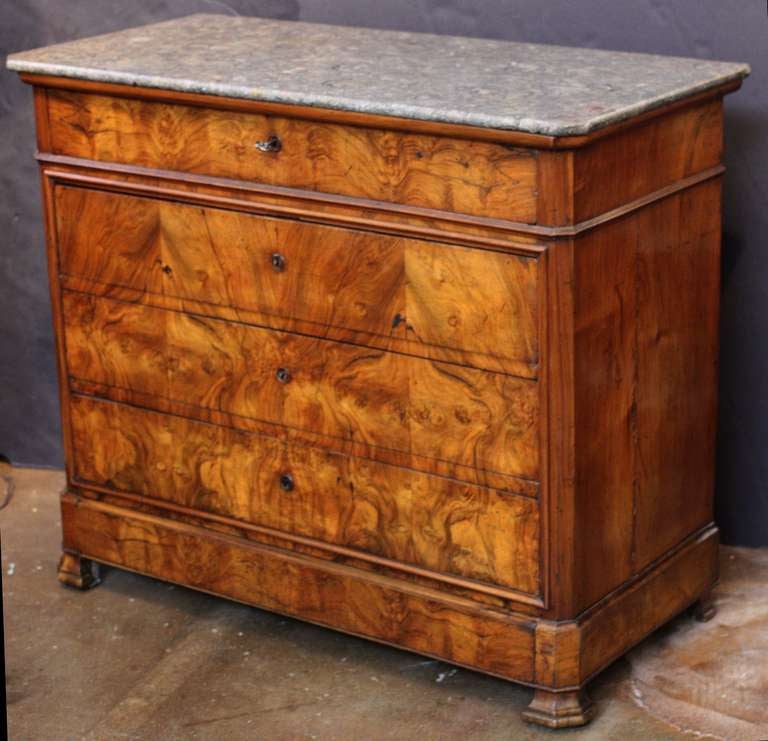 A handsome French chest of drawers in the Louis Philippe style, featuring a figured marble top set upon a chest of burled walnut with canted front. The chest with four long drawers of varying size (with key), each drawer with raised escutcheon.