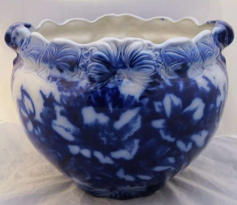 A beautiful large English flo-blue jardiniere or cache pot featuring a floral relief design around the top and handles, and floral transfer-ware design in flow blue.
