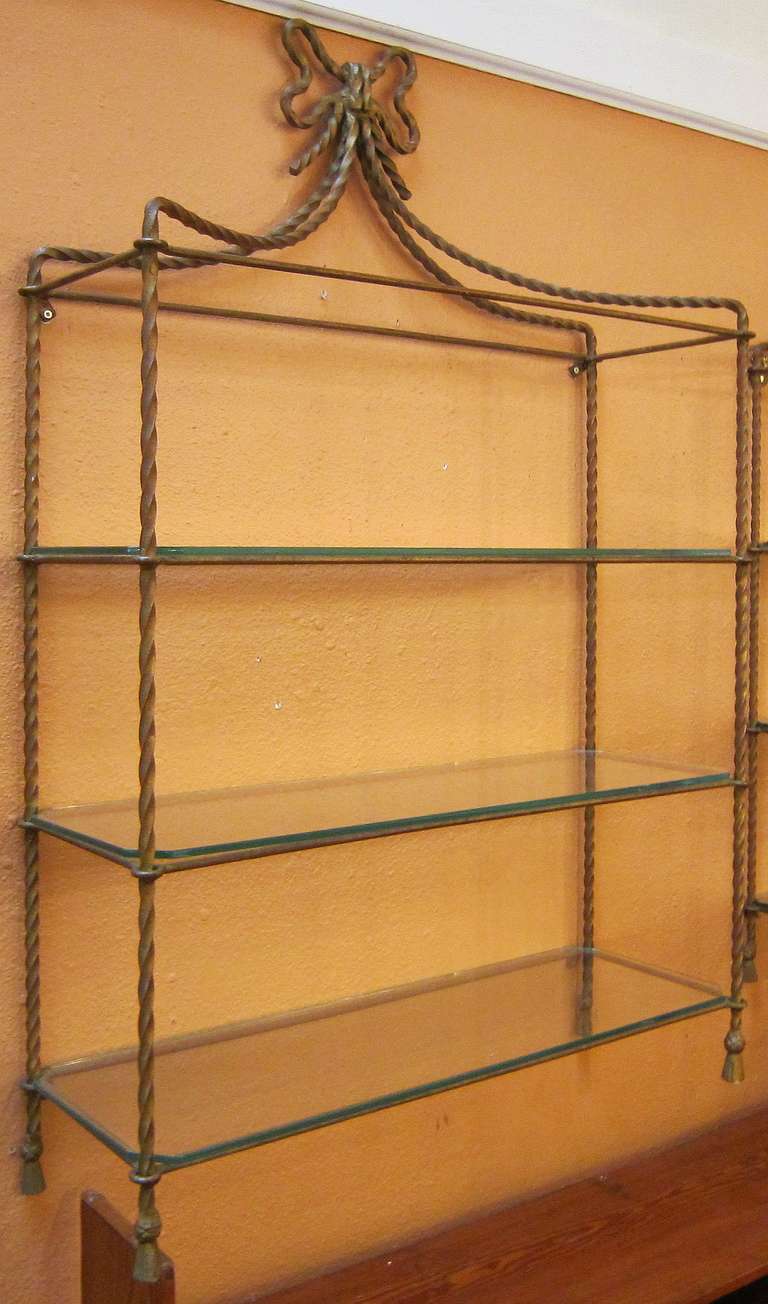 A handsome French gilt metal and glass hanging shelf, featuring a stylized ribbon frame of gilt metal, topped by a bow, with three removable glass shelves.


