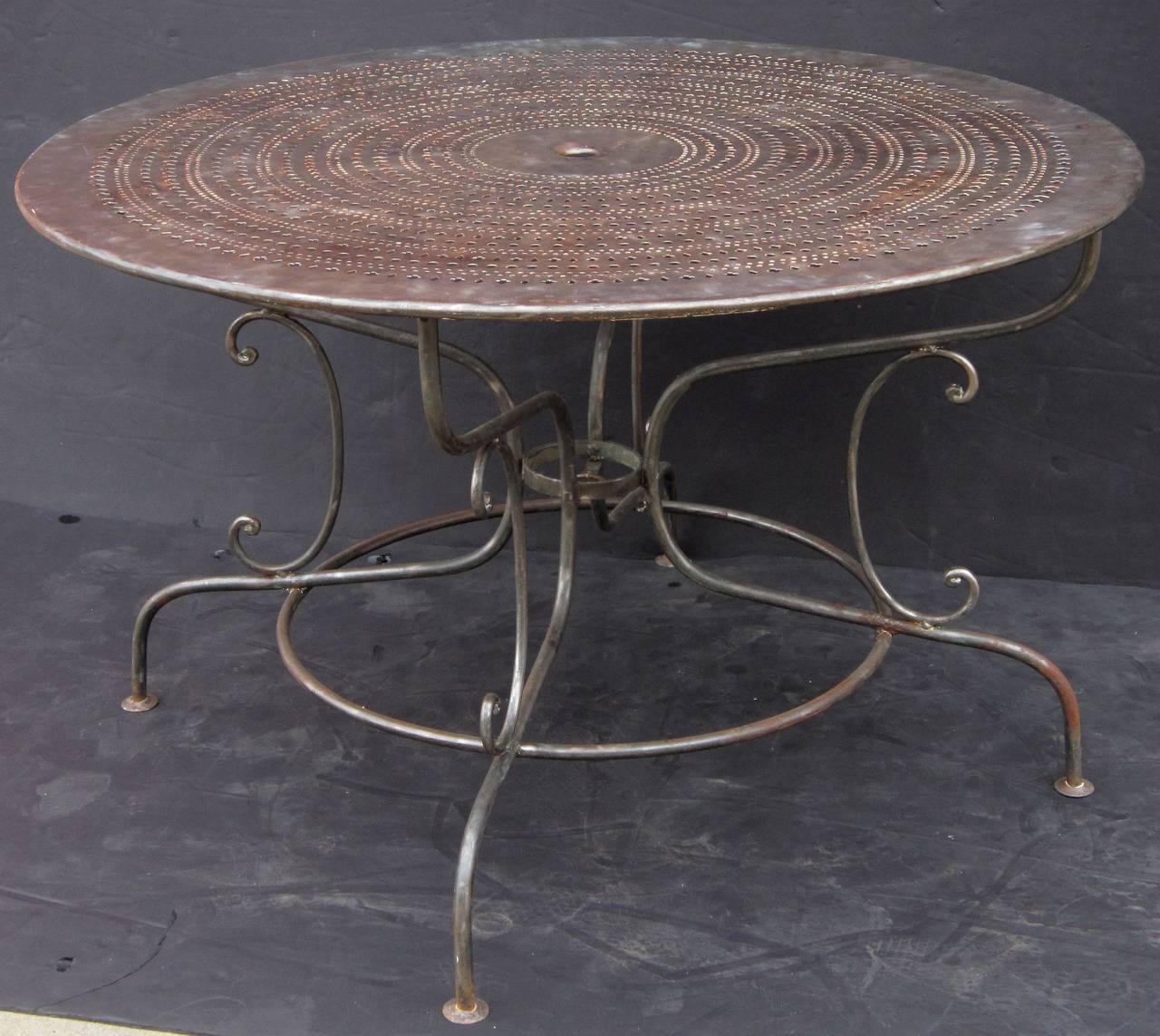 A large French café or bistro table of brushed steel featuring a round pierced pattern top with a lovely patina, attached to a stretcher base with serpentine legs.

Great for a patio or garden.