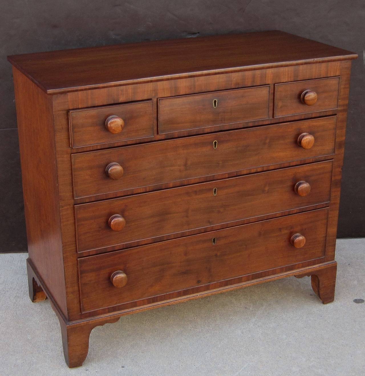 A fine English small chest of drawers of mahogany, featuring a moulded top over a frieze of three short drawers, two opposing with pull knobs over three long drawers with pull knobs. All with beaded fronts and a row of brass escutcheons through the