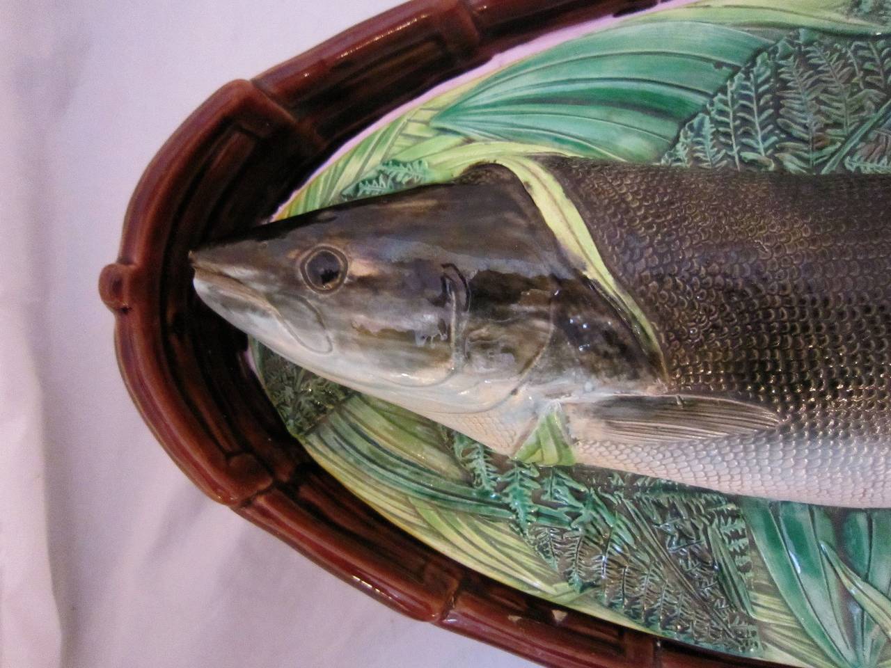 A fine Majolica fish server or salmon tureen by the celebrated English pottery firm, George Jones. The oval-shaped tureen featuring a relief on the lid of a salmon laying on a bed of ferns on the lid. The lid opening to a fitted, removable pierced