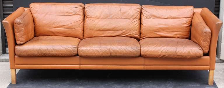 A period Danish modern three-seat sofa or settee (couch) of tanned leather with handsome, stylish design.
 
Featuring eight cushions (seat, back and side) on a stylish upholstered frame that offers great comfort as well as nice lines.
