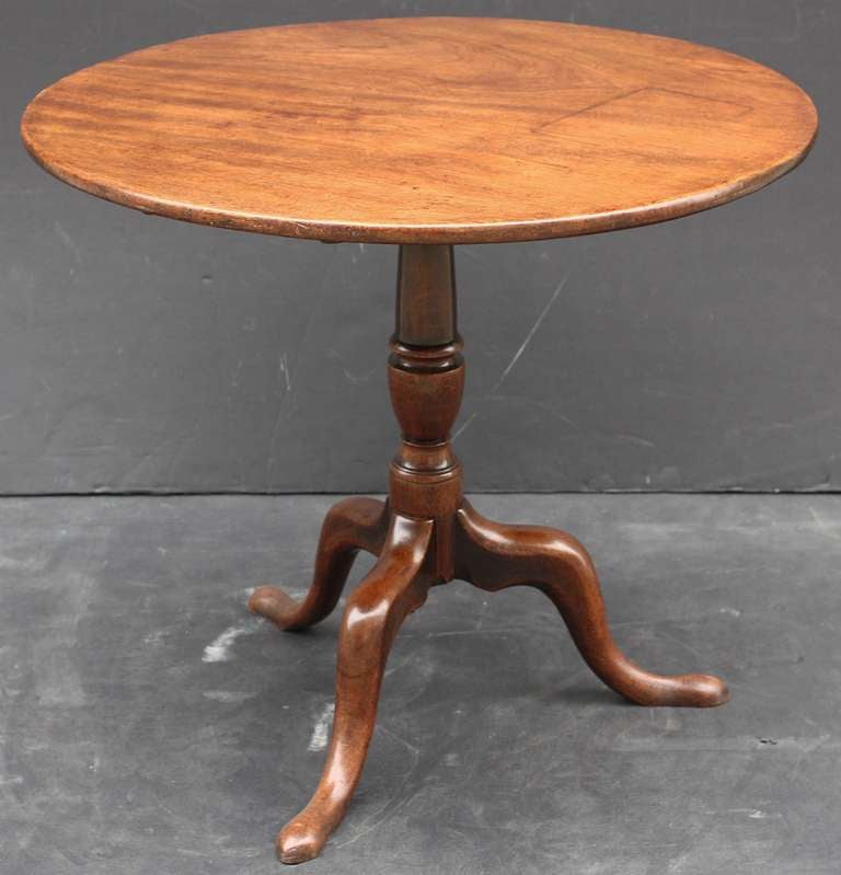 An English tilt-top table of mahogany featuring a round top mounted to a turned column pedestal with tripod base and pad-foot legs. With original brass hardware.