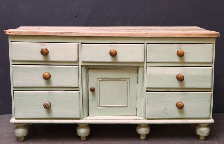 An English Country style cupboard console server or sideboard of painted pine, featuring a moulded pine top over a painted cabinet with seven drawers, each with wooden knob pulls, surrounding a recessed cupboard door, and set upon painted ball feet.