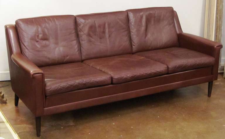 A period Danish Modern three-seat sofa or settee (couch) of dark brown tanned leather with handsome, stylish design.

Featuring six cushions (seat and back) on an upholstered frame that offers great comfort as well as nice lines.

Back Height