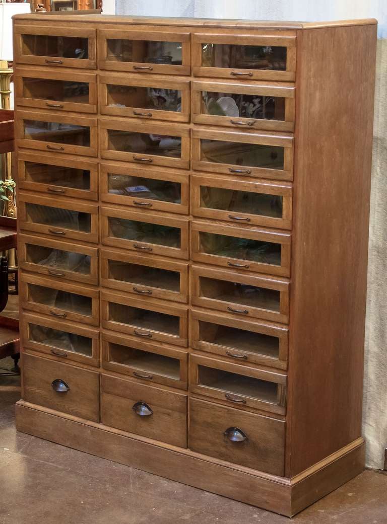 A haberdasher's cabinet from England featuring:

(24) glass-fronted drawers over (3) blind drawers - (27) drawers total.

Glass-front drawer inside dimensions:
Each drawer  H 5 1/2