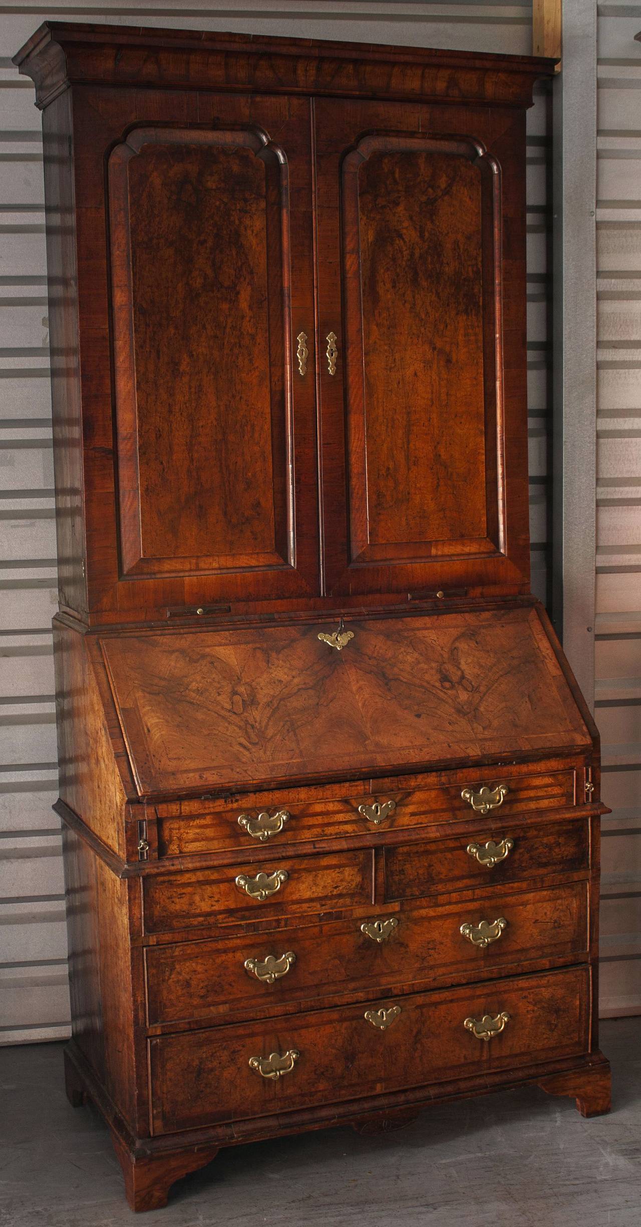 A fine English bureau bookcase secretary of burr walnut from the Georgian era, circa 1780, featuring an upper tier with canopy top over two paneled doors, enclosing three bookshelves.
The fall front enclosing a central cupboard flanked by secret