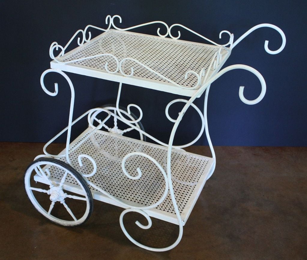 A Fin de Siècle-era drinks cart or serving trolley featuring two tiers of pierced metal joined by wrought metal scroll-work in a fanciful yet functional design - one that creates a gallery serving area on the top tier and bottle storage