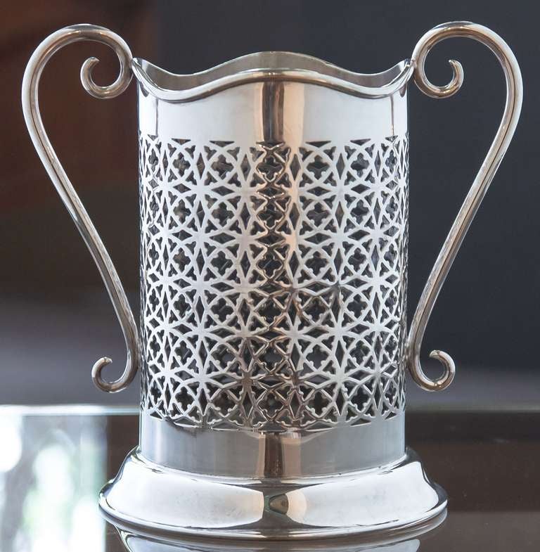An English wine bottle display holder or coaster of plate silver, featuring a pierced design around the circumference and opposing scroll handles, with rolled serpentine edge around the top.

Designed to add a fine level of elegance to the