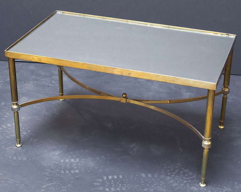 A handsome French rectangular low or coffee table (or cocktail table) featuring a stylish frame of brass on reeded legs, with mirrored glass top.