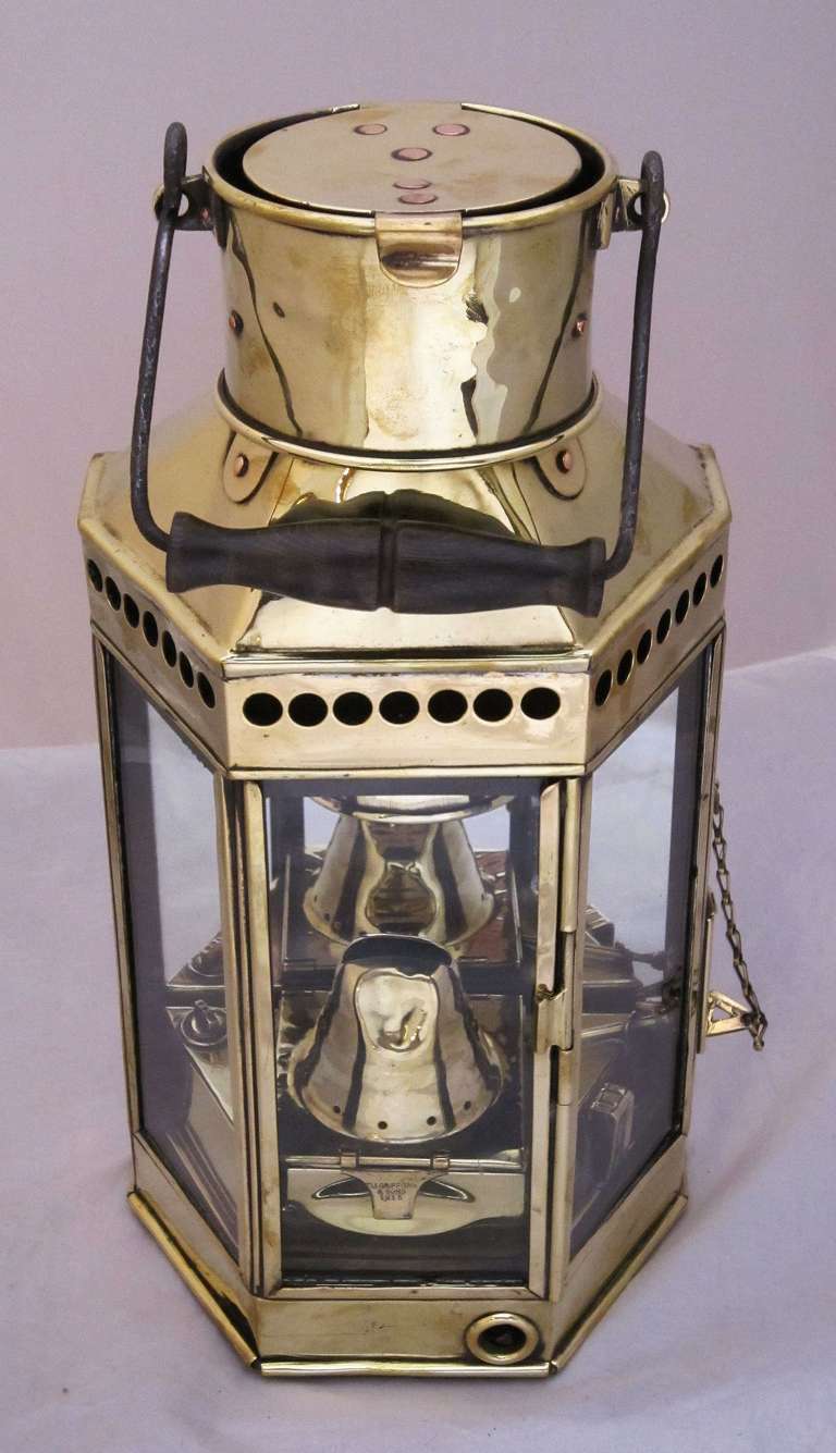 A handsome large English marine or nautical lantern of brass featuring a bail handle, flat back with hanging bracket, five-sided with three glass panes, including one with a hinged door, insert marked: Eli Griffiths & Sons, 1915
With hinged chimney
