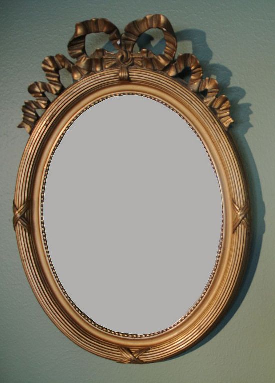 A pair of French oval (portrait) mirrors featuring frames of carved and gessoed wood, with gilt overlay and a ribbon and bow design crowning the tops.<br />
<br />
Priced as a pair. Available individually.
