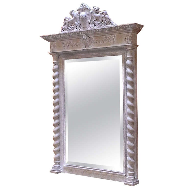 A handsome 18th c. French hall mirror of white-washed cherry wood, featuring a carved armorial above a frieze with scroll-work embellishments, flanked by two barley twist columns and framed mirrored glass.